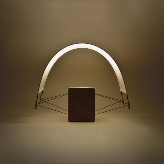 Vue de biais de la petite lampe à poser Écla de la Collection Aura créée par Maison Cédrat. Elle se compose d'un pied en brique et d'un abat jour en papier washi. La lampe est en finition terre crue cirée beige. allumée elle diffuse une lumière douce et dorée presque végétale dans une ambiance chaleureuse.