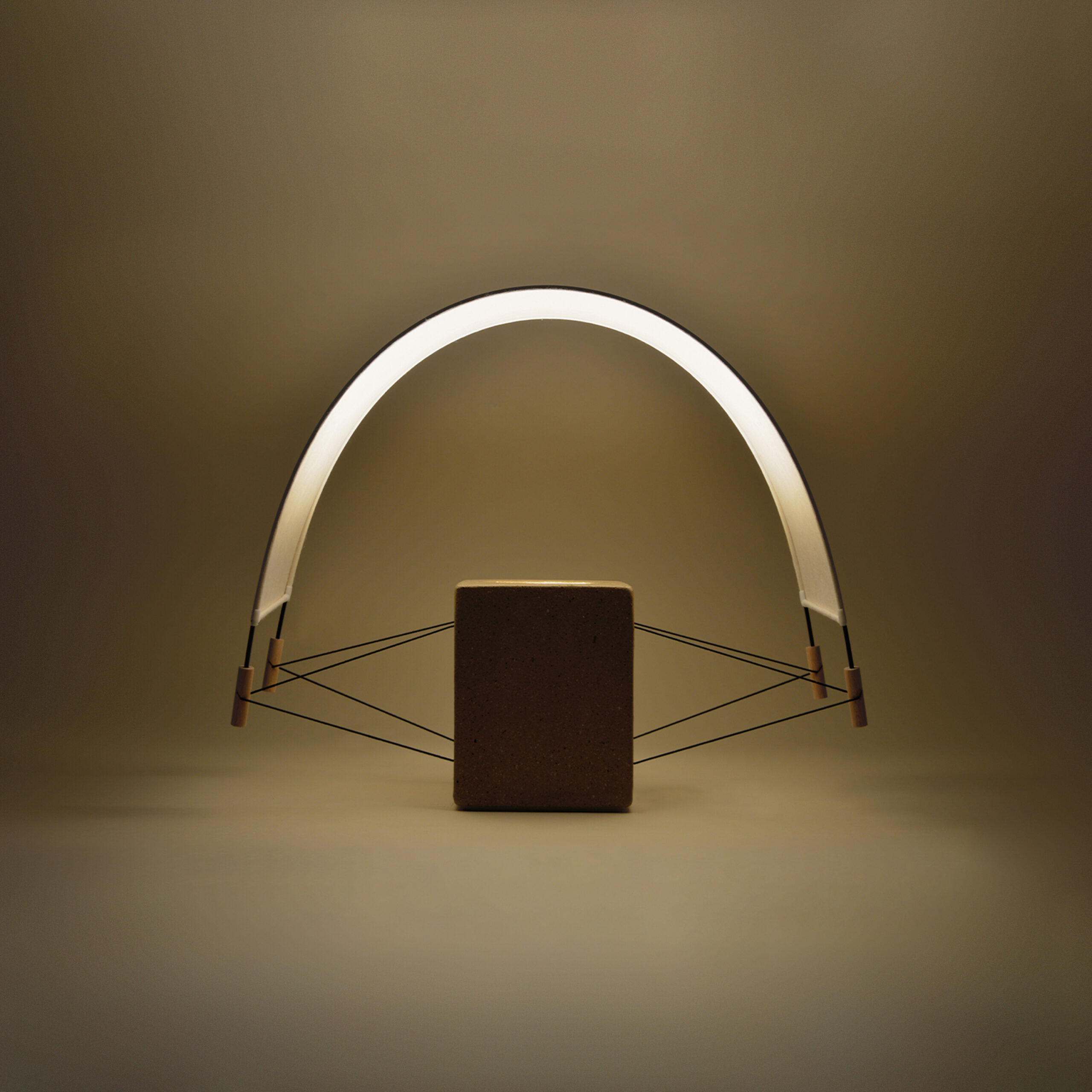 Vue de biais de la petite lampe à poser Écla de la Collection Aura créée par Maison Cédrat. Elle se compose d'un pied en brique et d'un abat jour en papier washi. La lampe est en finition terre crue cirée beige. allumée elle diffuse une lumière douce et dorée presque végétale dans une ambiance chaleureuse.
