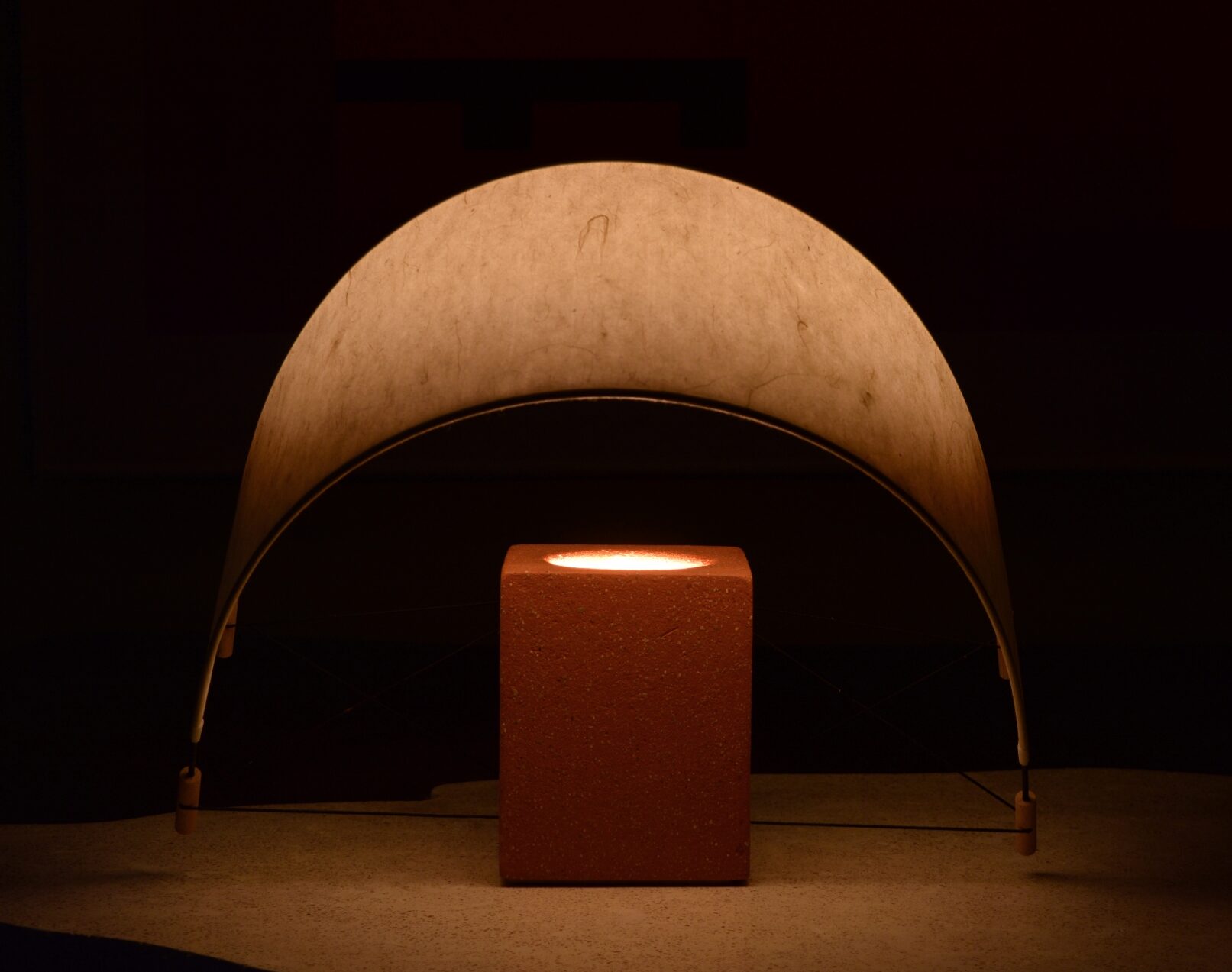 Écla Terracotta, petite lampe à poser allumée, en papier washi et terre cuite avec l'abat-jour incliné vers l'avant.