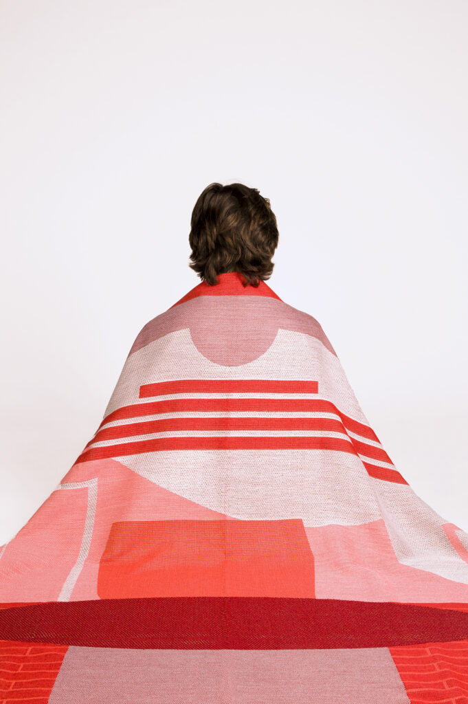 Étreinte, plaid en laine, tissage jacquard haut de gamme. Un subtil jeux d'armures révèles un motif géométrique. Vue portée du plaid.