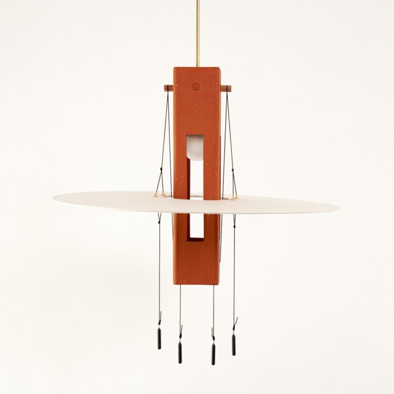 Photo de la suspension Nova , une piece en terre rouge suspendu autour de laquelle flotte un disque en papier japonais. Une suspension lumineuse créée par Maison Cédrat pour la Collection Aura.