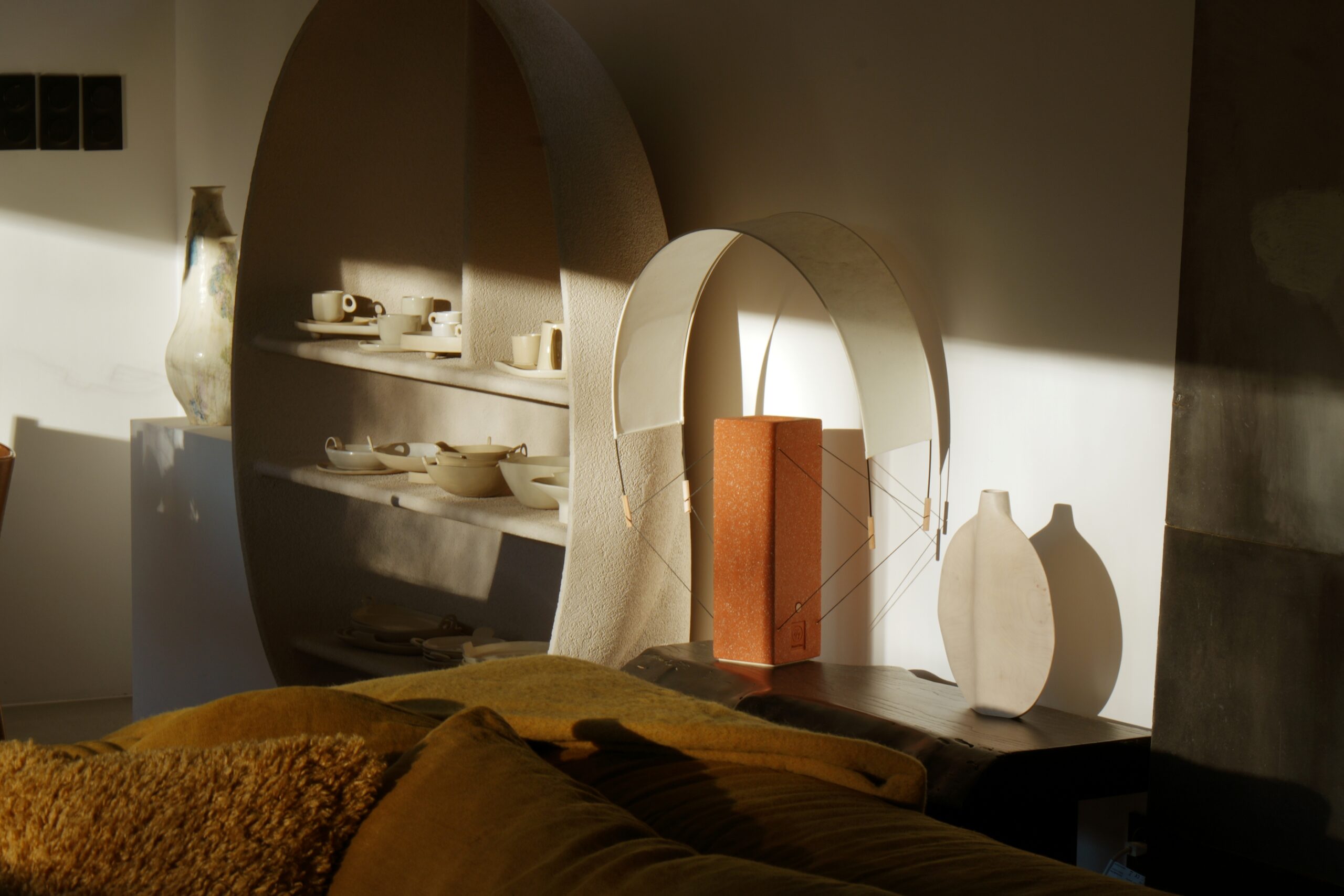 Photographie de la lampe à poser lumia en terre cuite avec un jeu d'ombres portées. Elle est entourée d'objets artisanaux design et contemporain et se marie à perfection dans se décor