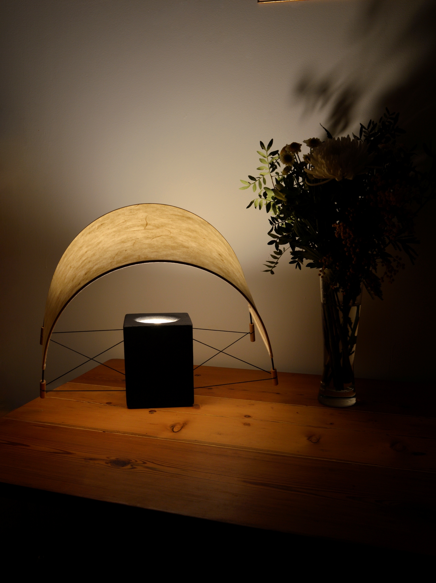 Lampe à poser Écla Noire allumée dans un chalet, avec son abat-jour en papier washi légèrement incliné vers l'avant.