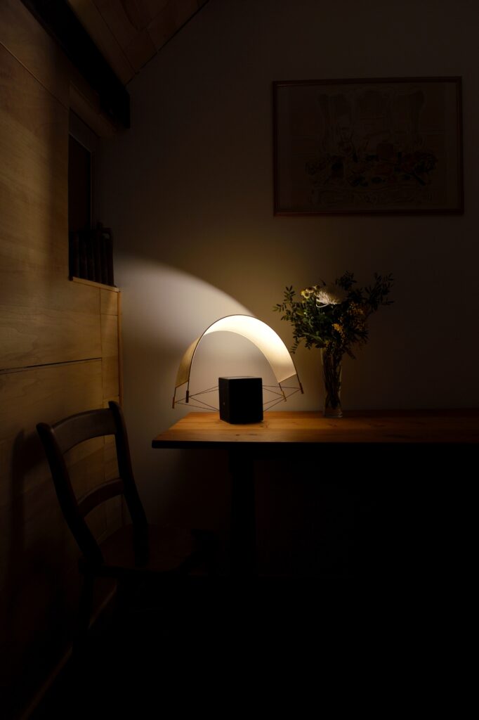 Écla Noire allumée avec la voile orientée vers l'arrière posée sur la table d'un chalet en bois. La lampe diffuse une lumière intime et chaleureuse.