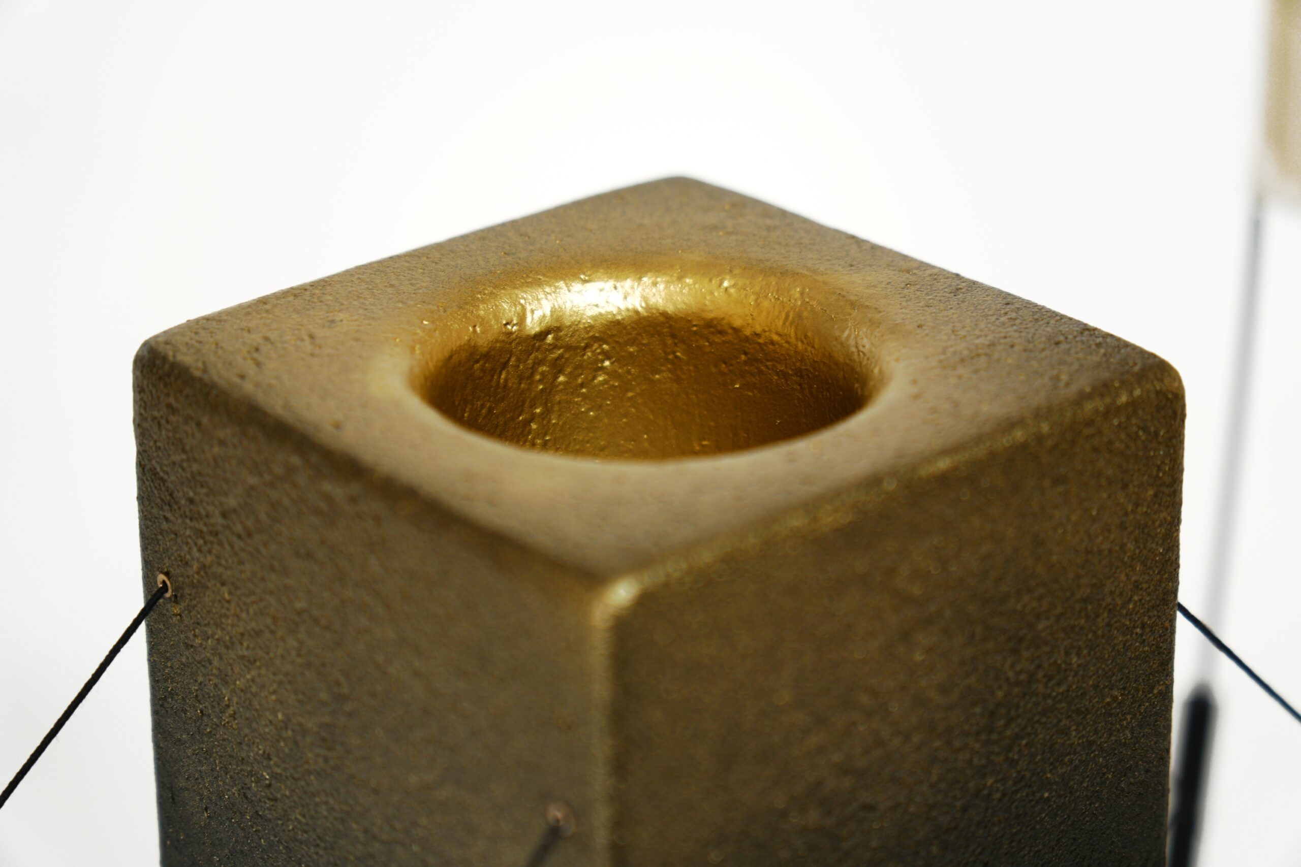Gros plan sur la finition dorée de la lampe à poser Lumia d'Or. Réalisée en pièce unique dans le cadre d'une collaboration avec le chocolatier Thierry Papereux, cette finition fait écho aux emblématiques Palets d'Or et révèle le caractère artisanal de la création.
