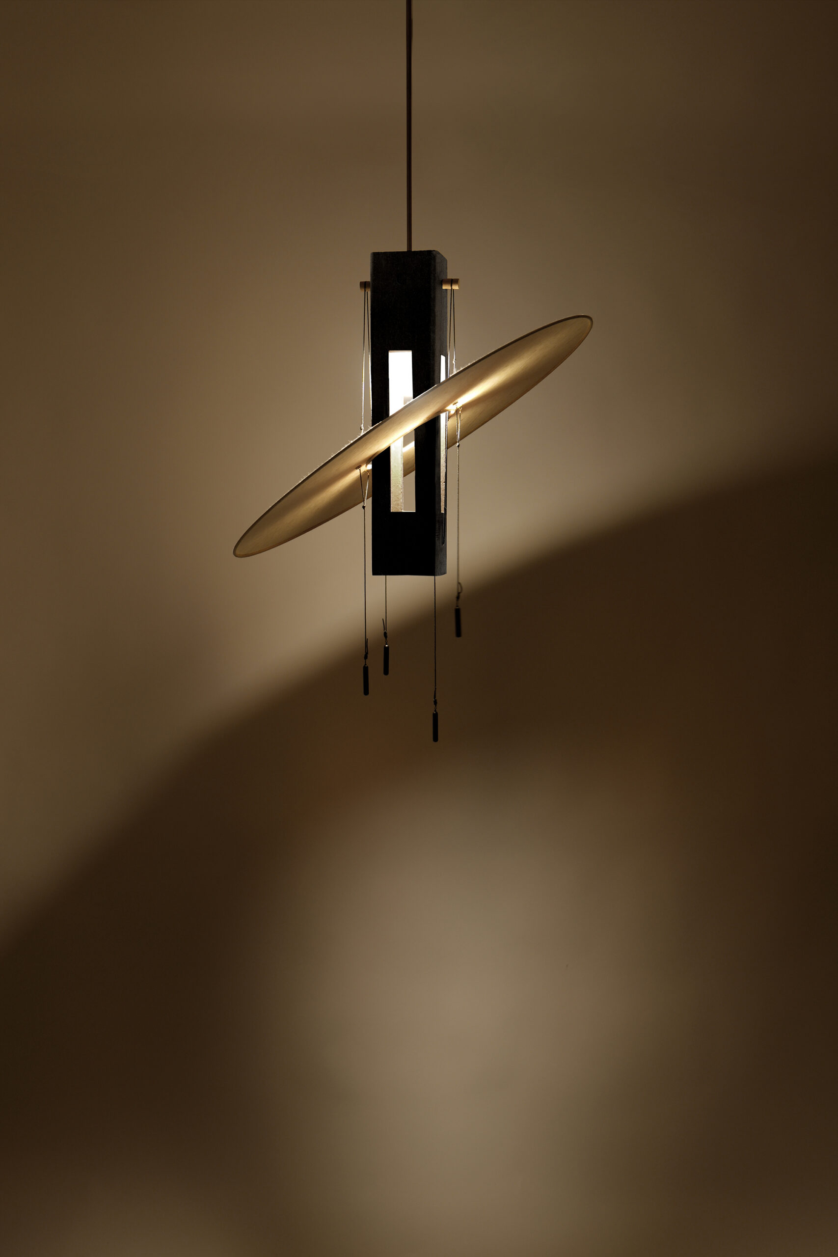 Nova Noire, suspension design éteinte, en terre peinte en noir et papier washi artisanal, de la Collection Aura par Maison Cédrat. Vue de la lampe allumée avec voile inclinée.