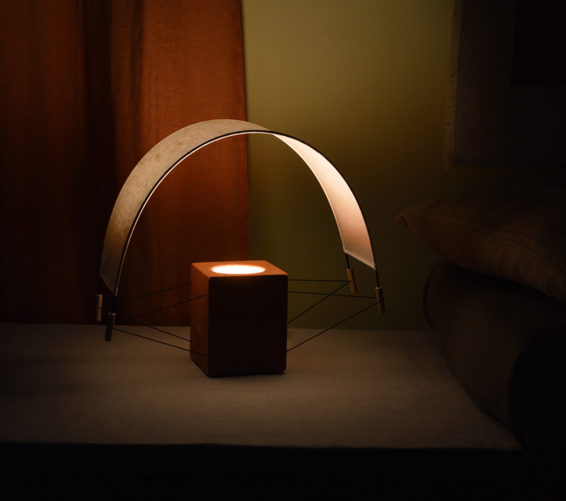 Photo de la lampe Ecla prise en biais à côté d'un canapé. Mise en scène de la lampe en finition terre cuite qui diffuse une lumière chaleureuse.